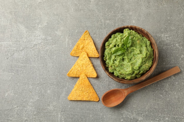 Bowl of guacamole, spoon and chips on gray background