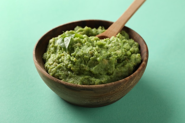 Bowl of guacamole with spoon on mint background, close up