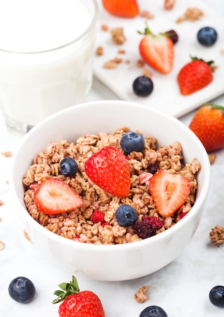 Ciotola di muesli di cereali sani con fragole e mirtilli e bicchiere di latte sul bordo di marmo