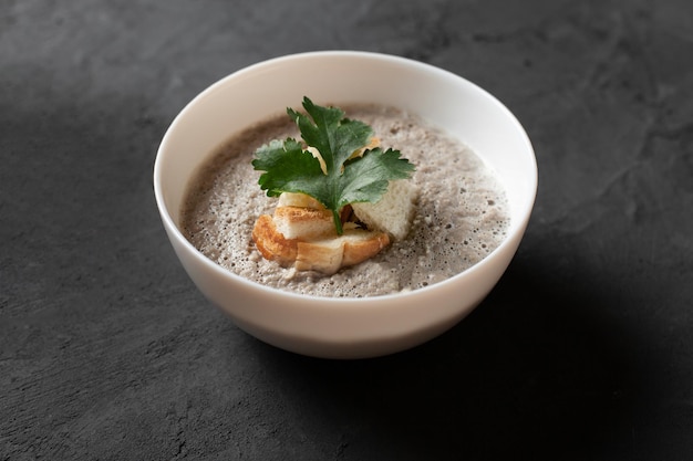 Bowl of homemade champignon mushrooms cream soup with croutons and parsley on concrete table