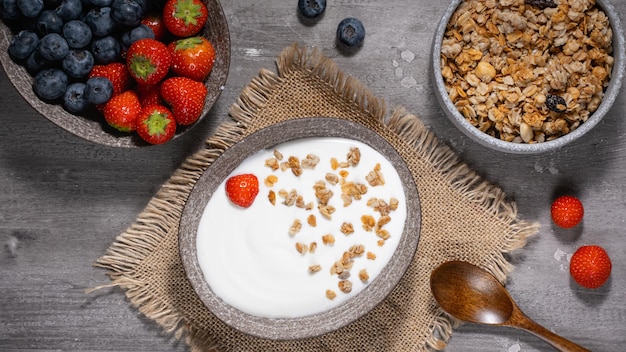 Bowl of homemade granola with yogurt and fresh berries on wooden background from top view