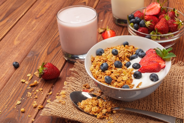 Bowl of homemade granola with yogurt and fresh berries on wooden