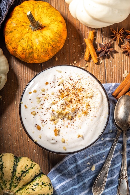 Bowl of homemade pumpkin spice yogurt ready for breakfast with tart crumble topping On wooden background with autumn pumpkins and spices copy space