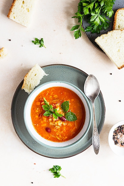 A bowl of homemade red bean and lentil soup, bread and parsley. Vegetable spicy soup.