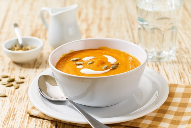 Чаша домашнего супа с органической тыквой со сливочным соусом на белом деревянном столе