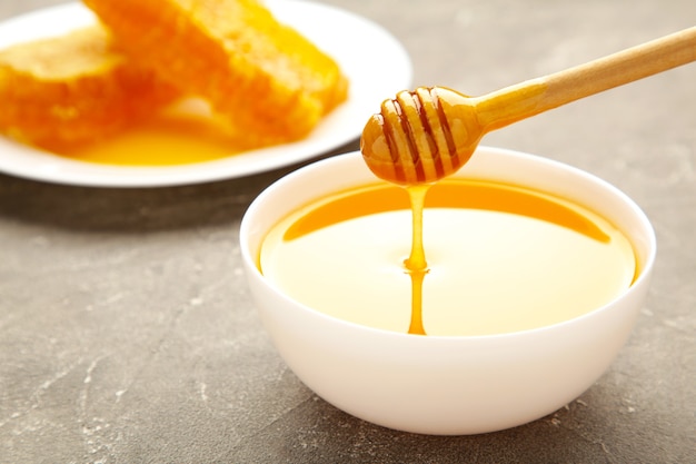 Bowl of honey with honeycomb on grey table. top view