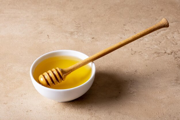 A bowl of honey and a wooden spoon for honey on a light surface