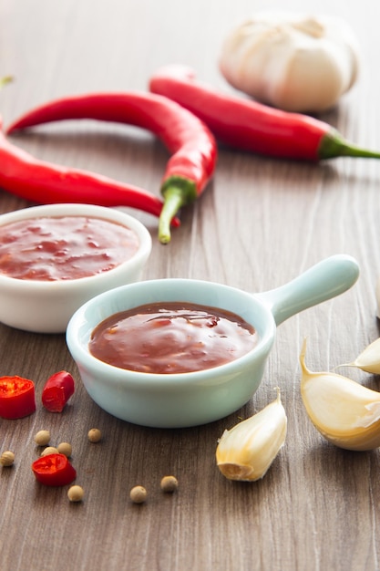 Bowl of hot chili sauce with red peppers on dark wooden background