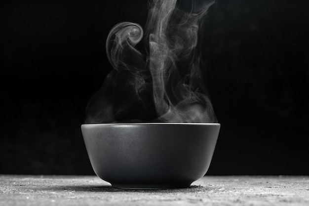 Bowl of hot steam of hot soup with smoke black ceramic bowl on dark background Hot food Culinary cooking concept