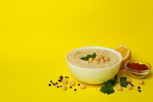 Bowl of hummus and ingredients on yellow