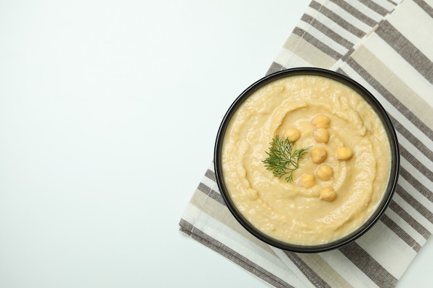 Bowl of hummus on kitchen towel on white surface