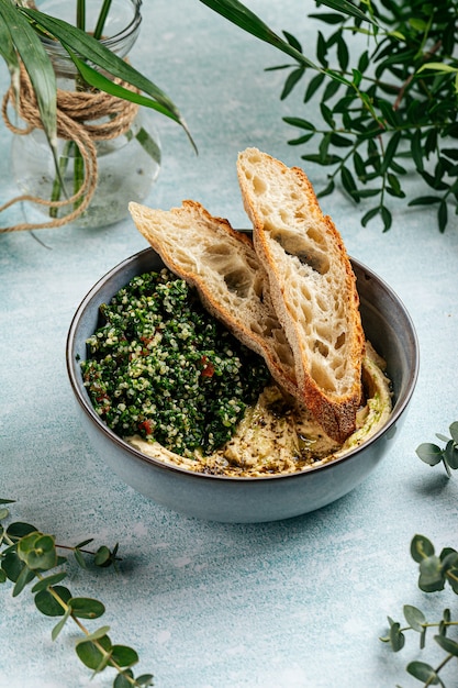 Bowl of hummus with tabbouleh salad and toasts on the blue background