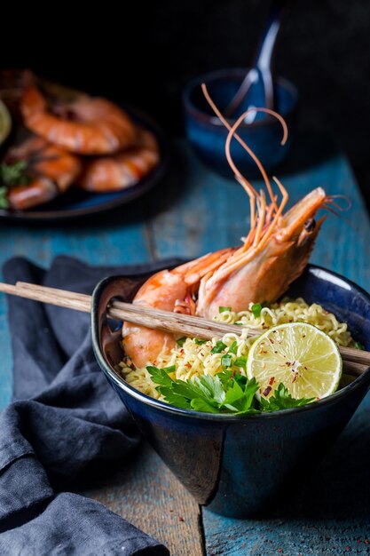 A bowl of instant Chinese noodles with green onions, red hot chilli peppers, and shrimps on a dark rustic background