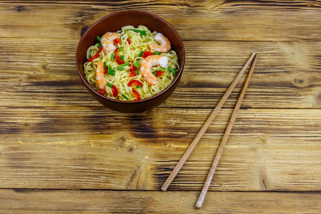 Bowl of instant Chinese noodles with shrimps green onion and red hot chilli peppers on wooden table Top view