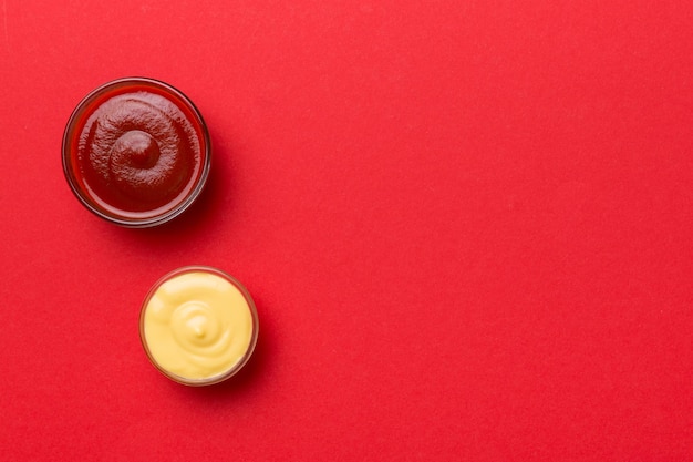 Bowl of ketchup and cheese sauce on colored background top view with copy space