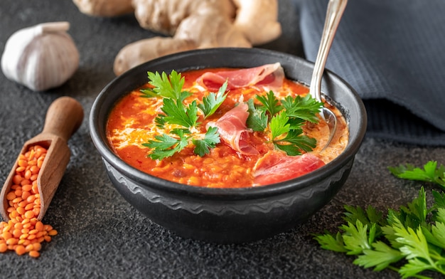Bowl of lentil tomato and coconut soup with sliced prosciutto