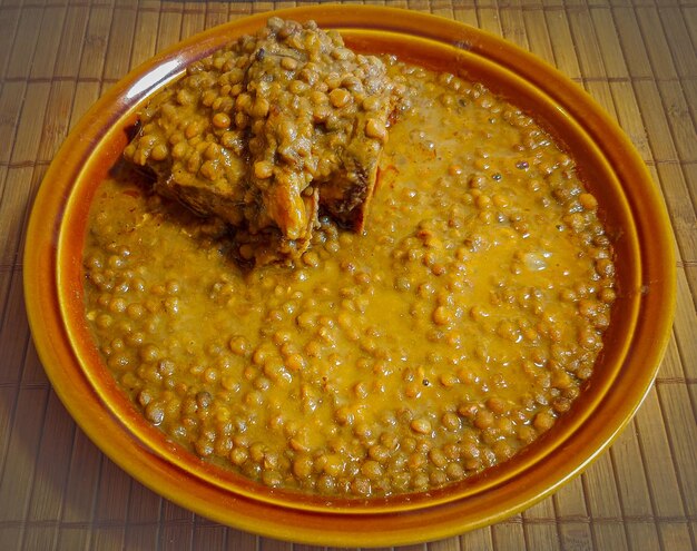 A bowl of lentils with a piece of meat on top of it.