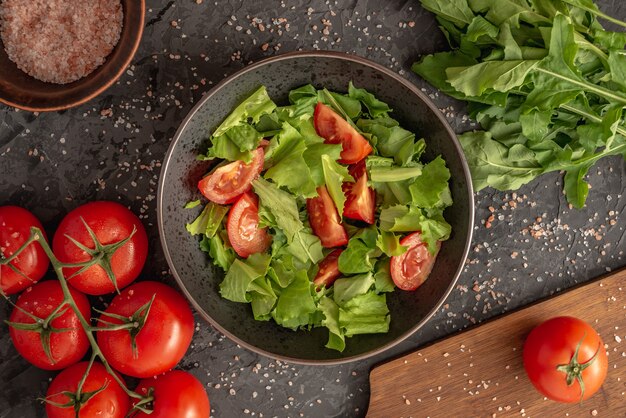 Bowl of light summer vegetable salad of tomatoes and greens and fresh ingredients for its cooking