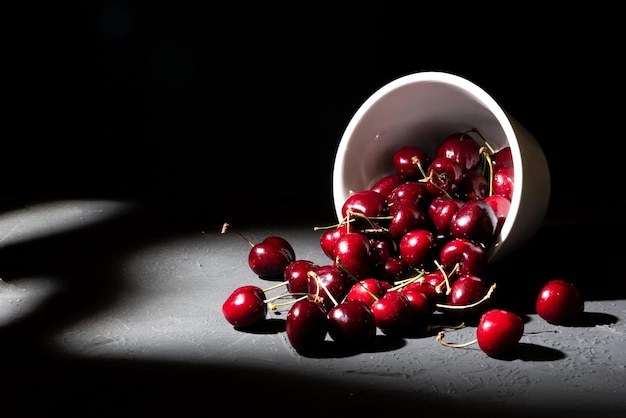 Photo bowl loaded with red cherries on dark background overturned cup spilling rich and healthy cherries