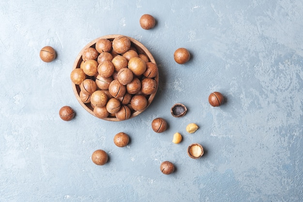 Bowl of macadamia nuts on a blue concrete table. Top view.