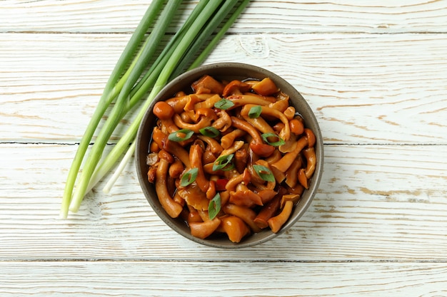 Bowl of marinated mushrooms on white wooden table