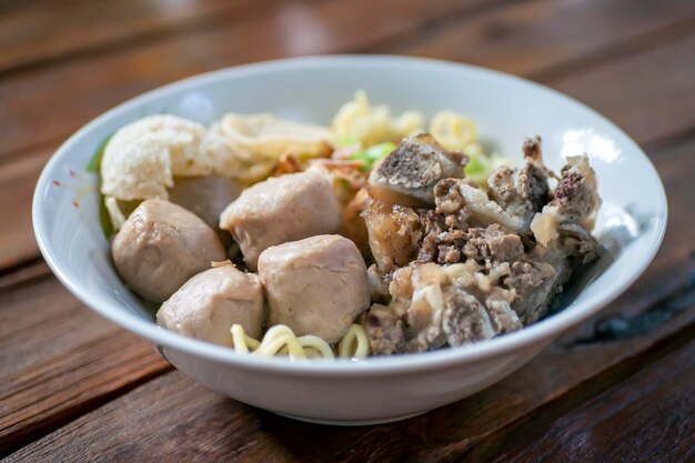 A bowl of meat ball soup with fresh vegetables on the old wooden table