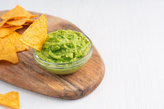 Bowl of mexican vegetarian guacamole sauce made of raw pureed avocado served with nachos on table