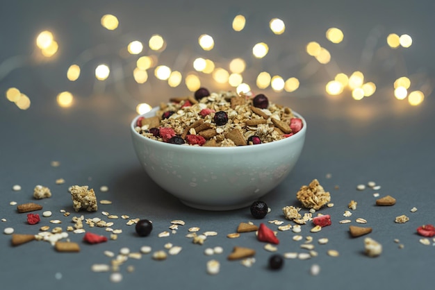 A bowl of muesli on a gray monochrome background, with white feathers and a side from a garland. Hea