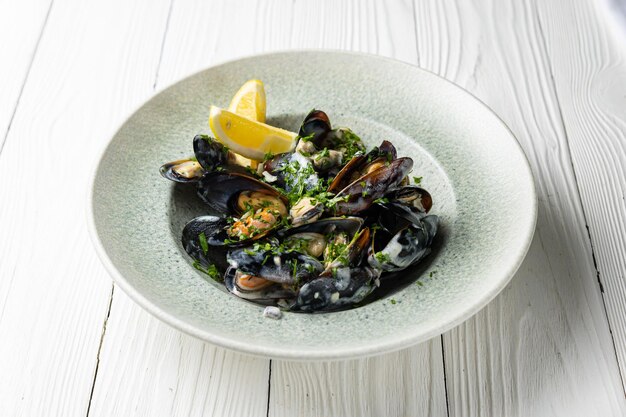 A bowl of mussels with lemon wedges on a white wooden table