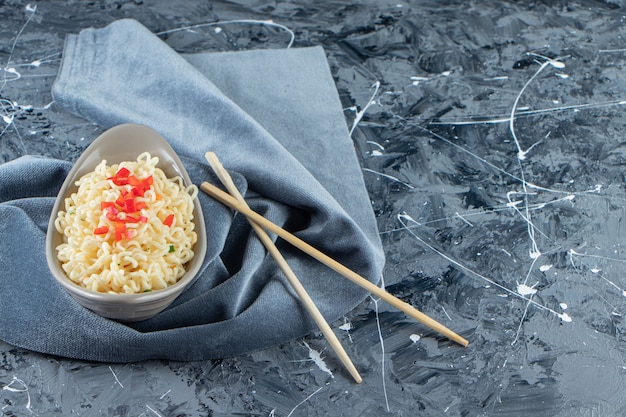 A bowl of noodle next to chopsticks on a pieces of fabric, on the marble background. 