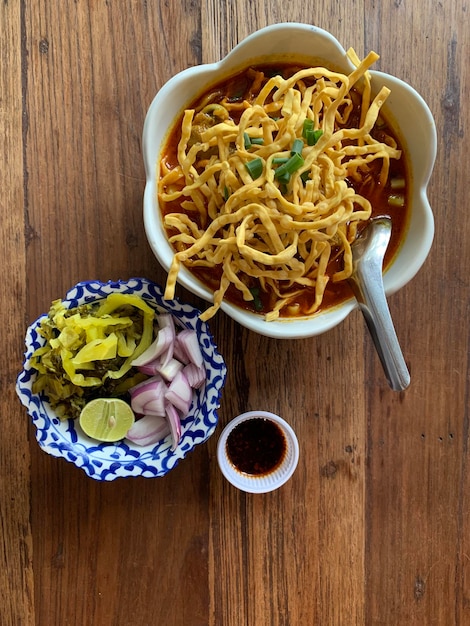 A bowl of noodles and a bowl of pickled vegetables are on a wooden table.