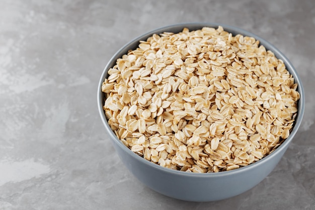 Bowl of oat flakes on gray background. Dry rolled oats in a gray bowl. Raw oatmeal flakes. Copy space. Top view