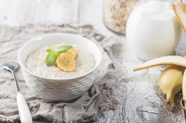 Bowl of oatmeal porridge with banana on white wooden rustic table, healthy breakfast, diet food.