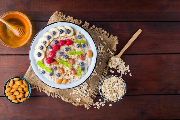 Bowl of oatmeal porridge with berries honey and fruits on burlap Tasty oatmeal with raspberries