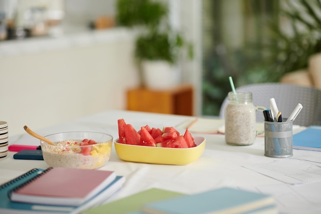 Bowl of oatmeal with fresh cut fruits on table with notebooks