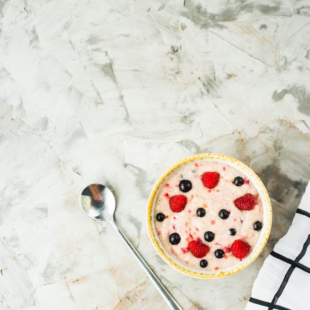 A bowl of oatmeal with raspberries and blueberries on a gray table 