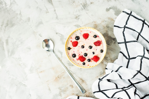 A bowl of oatmeal with raspberries and blueberries on a gray table 