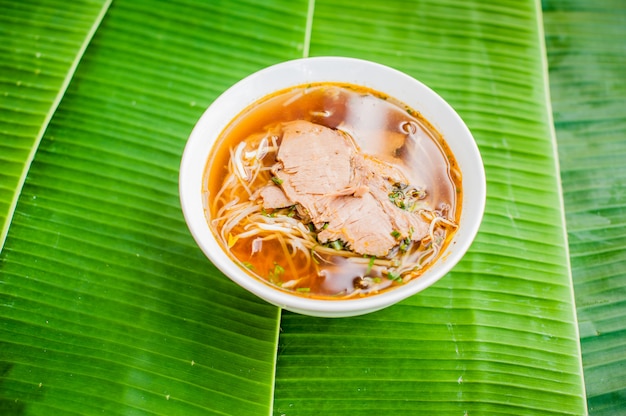 Чаша традиционный вьетнамский суп из говядины пхо бо на фоне банановых листьев.