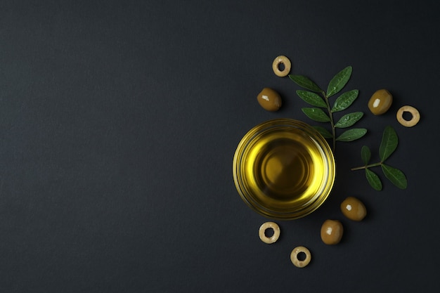 Bowl of oil, olives and twigs on black