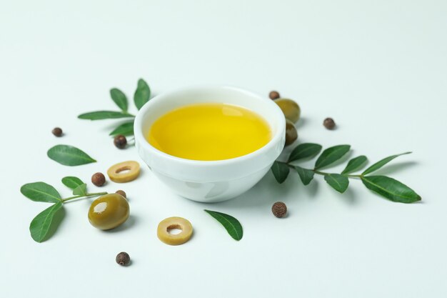 Bowl of oil, olives and twigs on white background