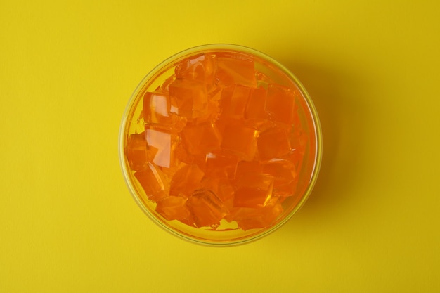 Bowl of orange jelly on yellow background, top view