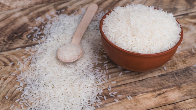 Photo bowl of organic white rice and wooden spoon over textured backdrop