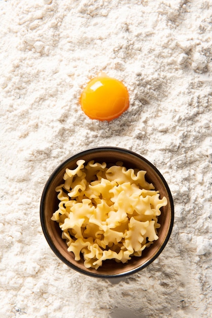 Photo bowl of pasta and egg yolk on flour.