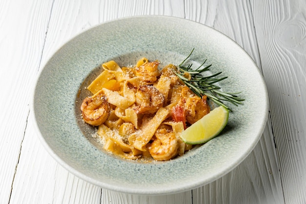 A bowl of pasta with shrimp and lime on a white wooden table.