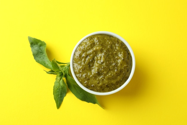 Bowl of Pesto sauce and basil on yellow background