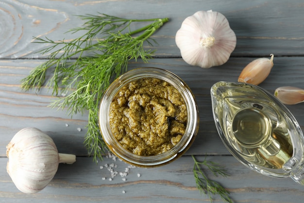 Bowl of pesto sauce, garlic, olive oil, salt on gray background, space for text. Top view