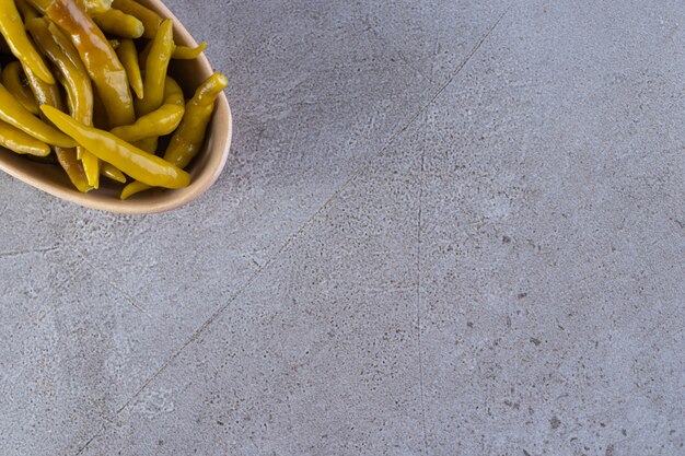 Bowl of pickled chili pepper placed on stone table.