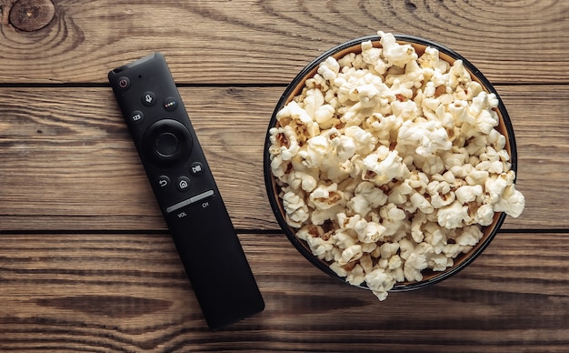 Bowl of popcorn, tv remote on wodden table.