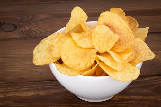 Bowl of potato chips on wooden background