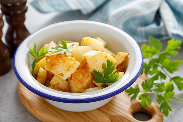 A bowl of potatoes with a blue rim sits on a wooden board